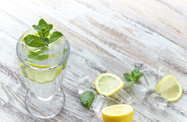 Water with lemon and mint in a glass container on a wooden table. place for text. refreshing summer citrus drink. vertical view of the summer drink.