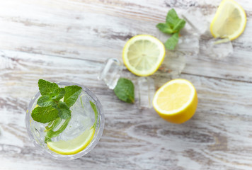 Water with lemon and mint in a glass container on a wooden table. place for text. refreshing summer citrus drink. vertical view of the summer drink.