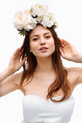 Beautiful young girl smiling and posing with flowers on white background in white dress. Studio portrait.