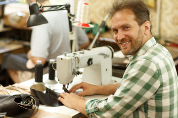Portrait of male specialist working with leather sewing machine at factory.