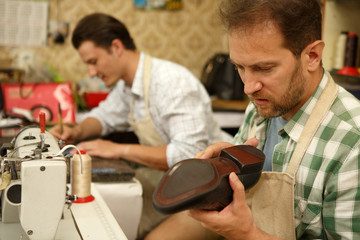 Two male specialists working on manufacturing leather shoes at factory.