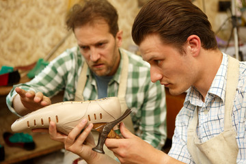 Senior tailor, showing colleague how to tighten leather on wooden shape.