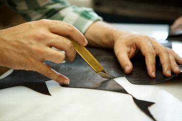 Obraz premium Shoemaker hand, cutting black leather with special knife at workshop.