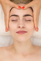 Obraz na płótnie Canvas Portrait of woman face with closed eyes relaxing during massage in spa salon. Hands of cosmetologist massaging attractive blonde lying on couch. Woman enjoying process of relaxing procedure .