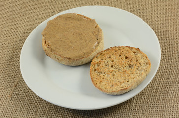 Almond butter on toasted English muffin on small white breakfast plate