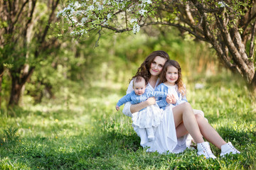 Obraz premium Portrait of young beautiful mother with two daughters near blossoming tree. Mother, two daughters in a spring garden.