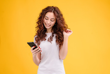 Fototapeta premium Attractive brunette girl with curly hair isolated over yellow background using mobile app for communication