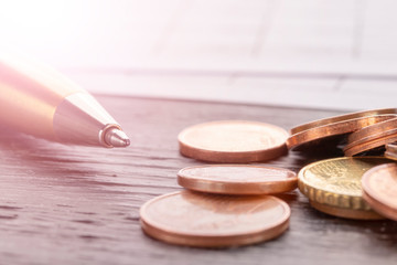 Stack of euro euro coins on old black wooden table. Pen and accounting documents with numbers