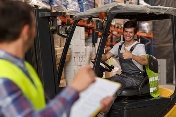 Manager of warehouse looking at loader, who smiling at him and showing thumb up. Forklift driver...