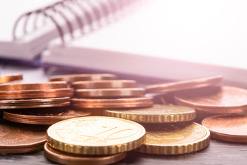 Stack of euro euro coins on old black wooden table. Pen, notebook