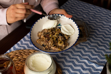 preperation of baked oatmeal with banana, blueberries, walnut and raisins. served with yoghurt and honey. dripping honey. putting yoghurt.