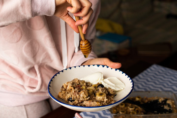 preperation of baked oatmeal with banana, blueberries, walnut and raisins. served with yoghurt and honey. dripping honey. putting yoghurt.