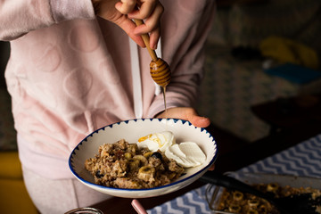 preperation of baked oatmeal with banana, blueberries, walnut and raisins. served with yoghurt and honey. dripping honey. putting yoghurt.