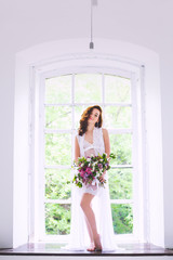 A young bride in a white shirt and a bouquet of flowers is on the windowsill