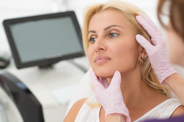 Closeup of woman face during procedure at cosmetology office. Beautiful female client looking away while doctor in gloves examining carefully skin after therapy. Concept of beauty and skin care.