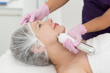 Closeup of satisfied female client lying on couch and enjoying cosmetic therapy in cosmetology office. Smiling woman relaxing during facelifting. Concept of skin care and cosmetology.