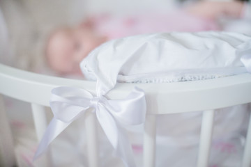 White bow on the pillow lying in the crib. White round bed newborn. Children's room decoration.