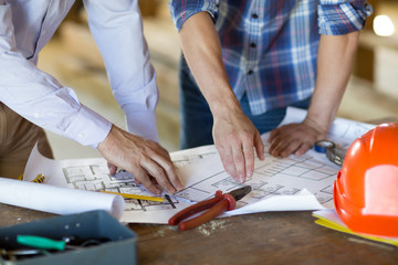 Close up of male contractor and client hand working with blueprint at table.
