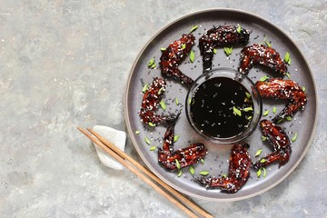 chicken teriyaki wings on a gray plate in a loft style on a concrete background and flowering plum twigs. Asian modern style. top view. copy space 