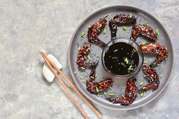chicken teriyaki wings on a gray plate in a loft style on a concrete background and flowering plum twigs. Asian modern style. top view. copy space 