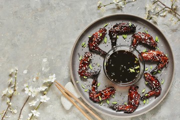 chicken teriyaki wings on a gray plate in a loft style on a concrete background and flowering plum twigs. Asian modern style. top view. copy space 