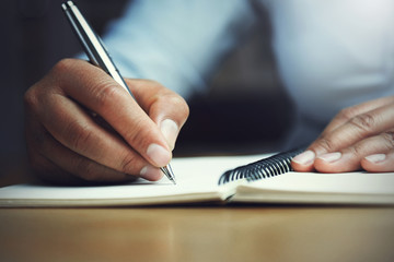 hand of woman holding pen with writing on notebook in office