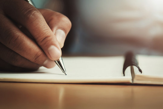 Hand Of Woman Holding Pen With Writing On Notebook In Office