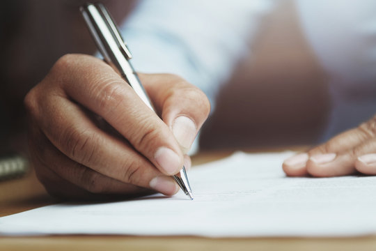 hand of woman holding pen with writing on paper report in office