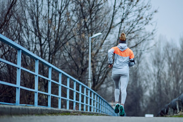 Rear view of determined sportswoman running on a road during cold weather.