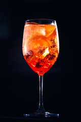 Stylish alcoholic aperol spritz cocktail with orange slice on black background.