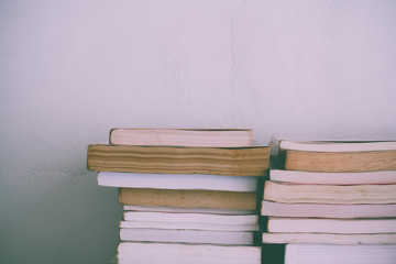 Stack of many old books on shelf in book store or library room with white wall background. Knowledge learning, education, bachelor degree in university or back to school concept.