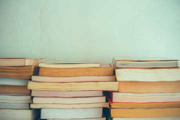 Stack of many old books on shelf in book store or library room with white wall background, vintage tone. Knowledge learning, education, bachelor degree in university or back to school concept.