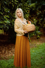 Sensual blonde woman in a brown dress European appearance with a wicker basket of citrus fruits standing in a green garden