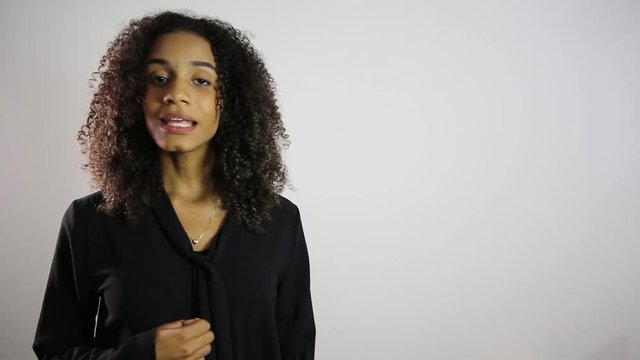 Young American Afro woman looking at camera talking and showing to the side presenting blank copy space for your text or product. Over white background. you can do a dubbing.