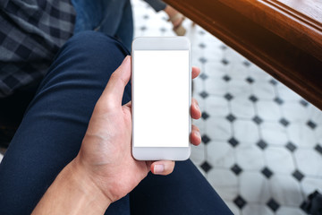 Mockup image of a man's hand holding white mobile phone with blank desktop screen on thigh in cafe