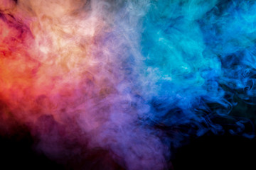 Obraz na płótnie Canvas Translucent, thick smoke, illuminated by light against a dark background, divided into three colors: blue, green, pink and purple, burns out, evaporating from a steam of vape for print on t-shirt