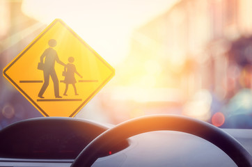 School zone warning sign and inside car view ,steering wheel on blur traffic road with colorful...