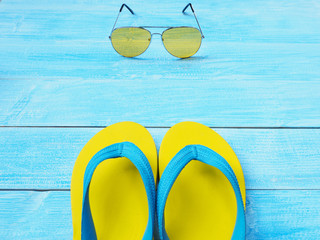 yellow flip flop shoes and sunglasses on blue wooden background