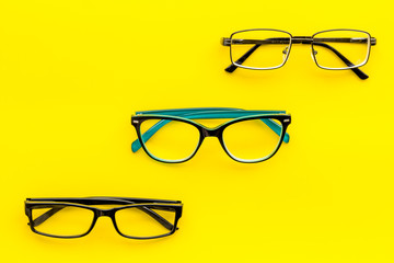 Set of glasses with transparent lenses on yellow background top view copy space