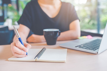 Business woman's hand is writing on a notebook with a pen.