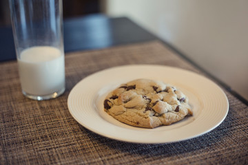 Closeup of a Delicious Chocolate Chip cookie on a plate sitting on a table next two a glass of milk