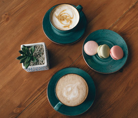 on a wooden table, two cups of coffee, macaroon and flower in a pot