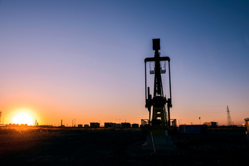 Oil pumps are running in the sunset at the oil field. The outline of the pumping unit.