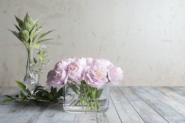 flower arrangement, flowers with leaves and a blooming twig are standing on old wooden boards against a single wall, in glassware