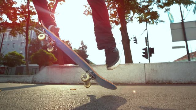 SLOW MOTION, CLOSE UP, LENS FLARE: Cool skateboarder riding through the city lands a fakie kickflip. Unrecognizable male skateboarder landing a difficult kickflip while enjoying his summer at the park
