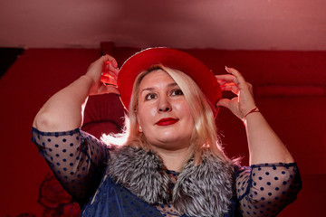 Fat woman wearing a hat in a dark room with red light. Gangsters style