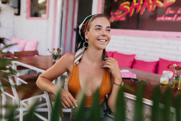 Happy laughing girl sitting on open-air summer terrace with pink sits, resting outdoor and waiting for date. Stylish attractive woman spend free time outside