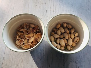 Pistachios and nut shells in two bowls on wooden table