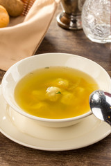 Low fat chicken broth with meatball in a glass bowl on wooden table
