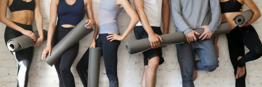 Group people wearing activewear holding yoga mats standing near wall 